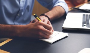 a man taking notes next to a laptop computer